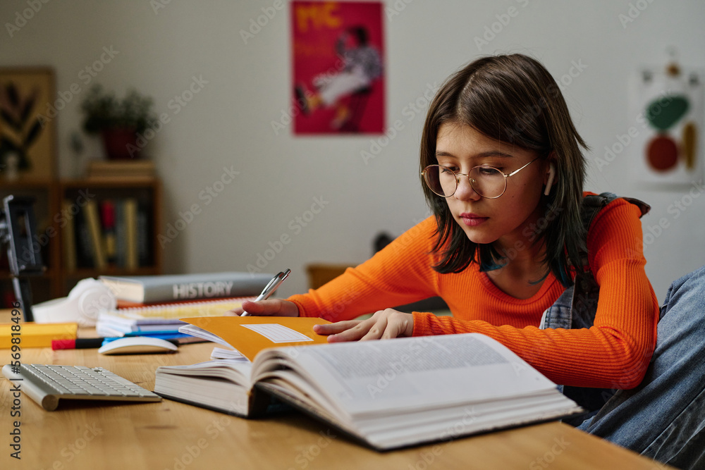 Teenage girl sitting at desk with books and notebooks and doing homework in her room Teenage girl sitting at desk with books and notebooks and doing homework in her room