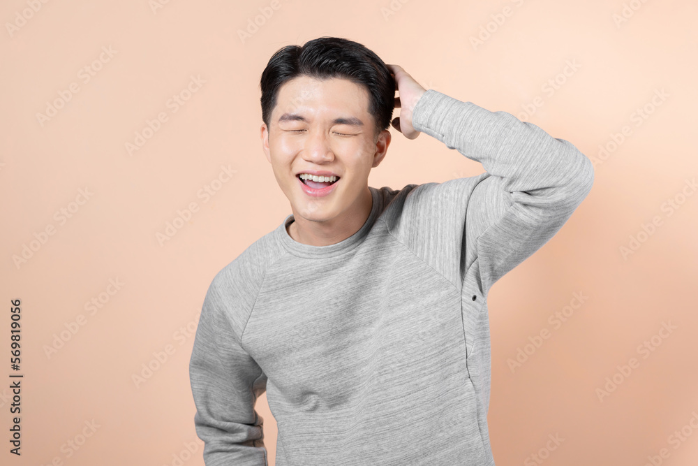 Portrait of a asian man touching his hair and laughing on beige background Portrait of a asian man touching his hair and laughing on beige background