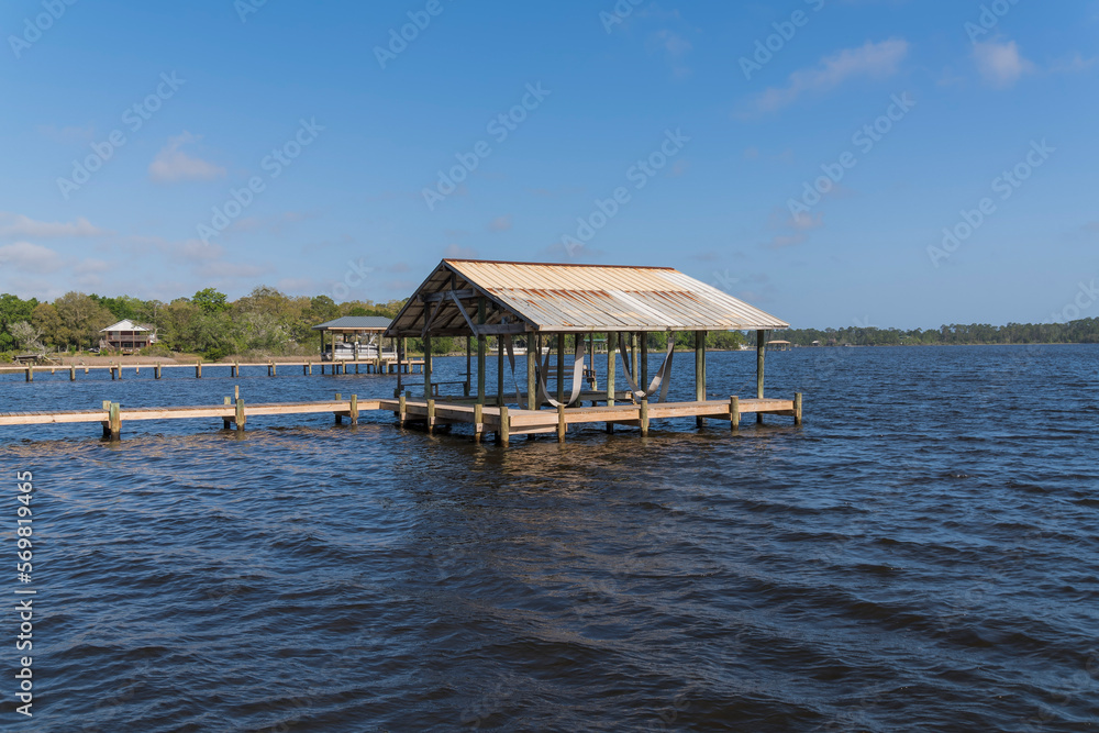 Empty boat lift with roof on a river at Navarre, Florida. Two boat docks with lifts against the shore with few villas surrounded by trees and clear sky background.