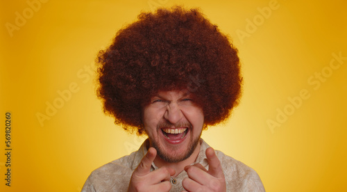 Joyful man with lush Afro hairstyle coiffure laughing out loud after hearing ridiculous anecdote, funny joke, feeling carefree amused, positive people lifestyle. Young hipster guy on yellow background © Andrii Iemelianenko