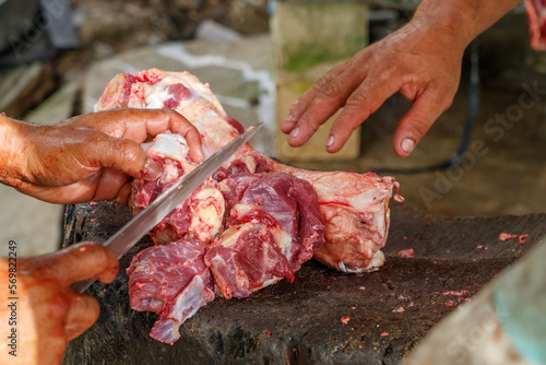 Male farmers in the countryside cut up pieces of beef.