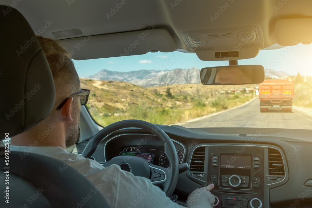 Fototapeta premium Person driving car, driver at the wheel adjusts the volume of the music and drives along a country road.