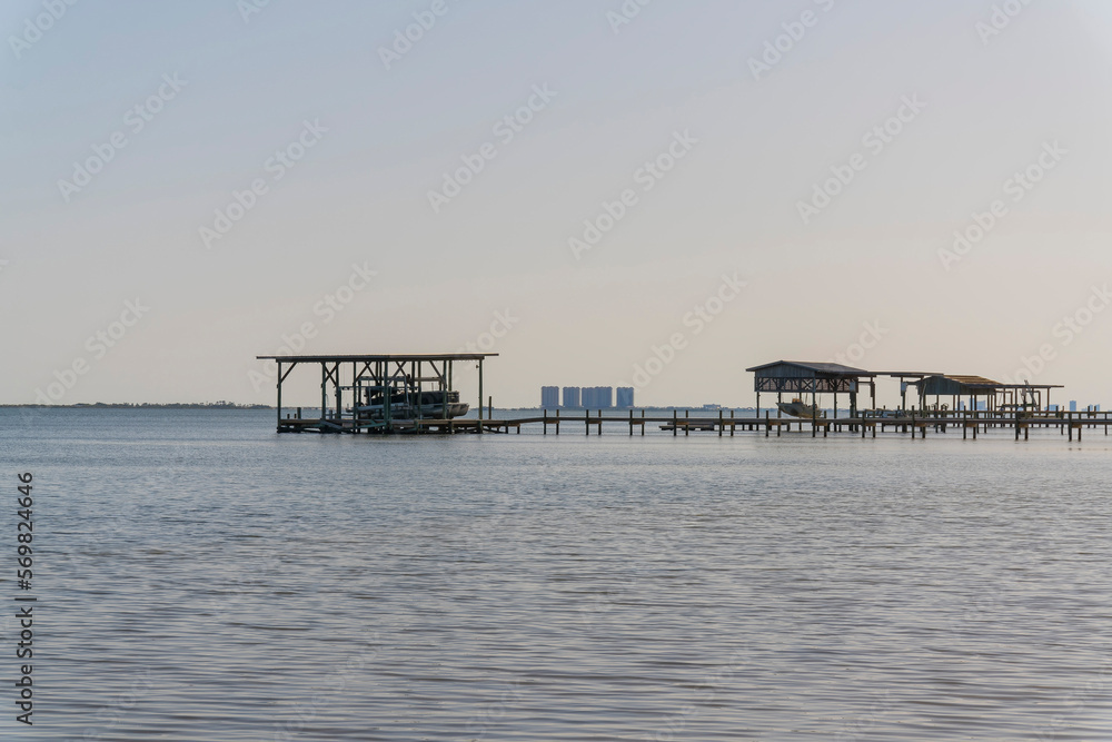 Wooden dock with boat lifts on the sea at Navarre, Florida. Views of boat docks with roofs against the sky and buildings at the background.