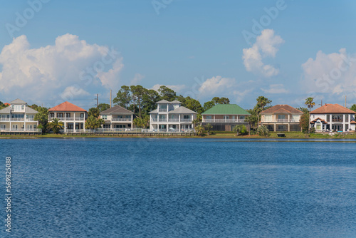 Facade of single-family homes with views of Four Prong Lake waterfront in Destin, Florida. Row of houses with balconies and fences against the giant pastel clouds in the sky background.