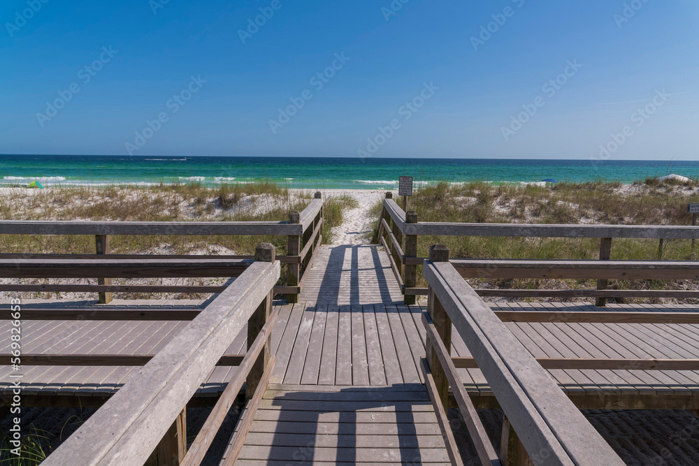 Wooden walkway on the beach in Destin Florida with view of the ocean and sky. Scenic coastal landscape with platform that overlooks the peaceful nature scenery on a sunny day.