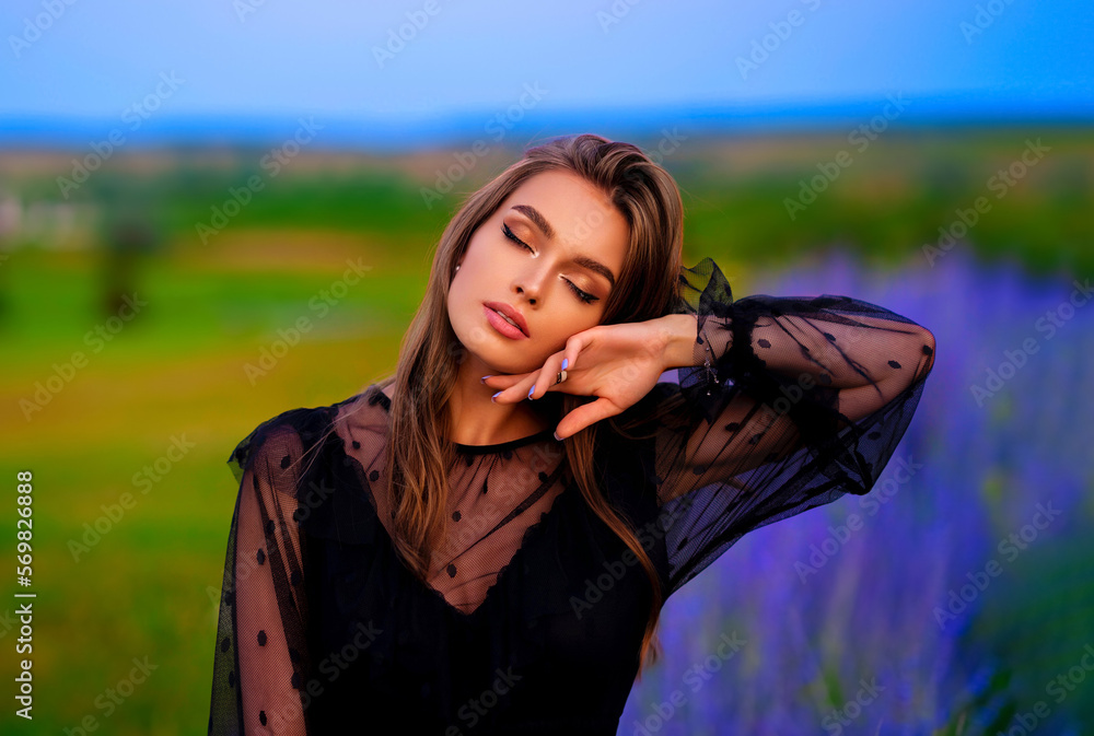 Portrait of a Beautiful smiling girl in a black transparent dress and straw big hat standing in colorful lavender field. Art work of romantic woman .Pretty tenderness model with close eyes.