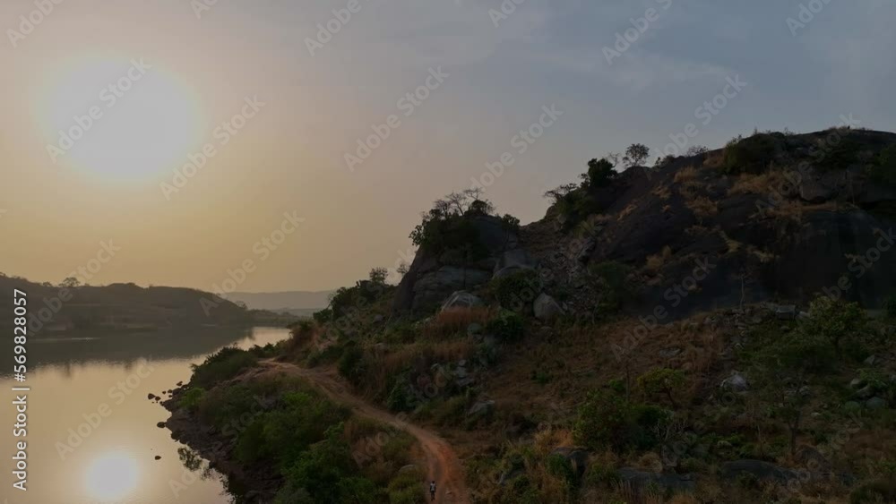 Aerial - Descending wide shot of a man walking on a dirt road at sunset Aerial - Descending wide shot of a man walking on a dirt road at sunset