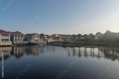 Decorative lake with reflections of the waterfront houses in Destin, Florida. There is a lake at front with water fountain near houses with decks and balconies on the left and palm trees on the right.