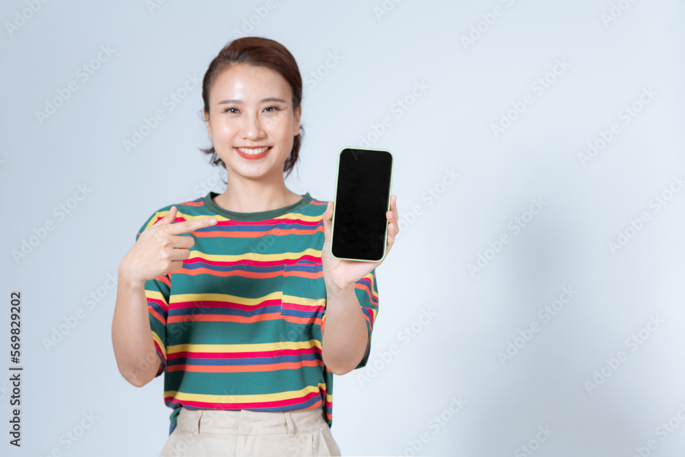 Beautiful Asian woman smile holding a smartphone on hand and pointing finger to the blank screen