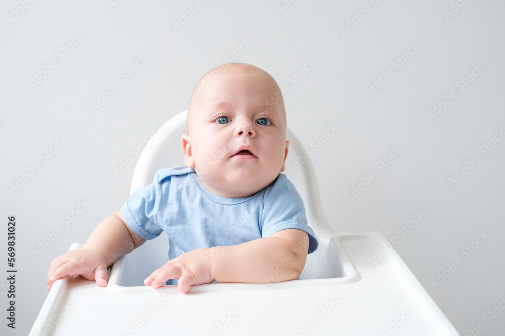 bald smiling baby boy 3 months sitting in baby chair on white background
