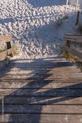 Perspective view of stairs from above heading to the white sand ground in Destin, Florida. Steps of a stairs with horizontal wood planks and sands partialy covering the bottom steps. photo