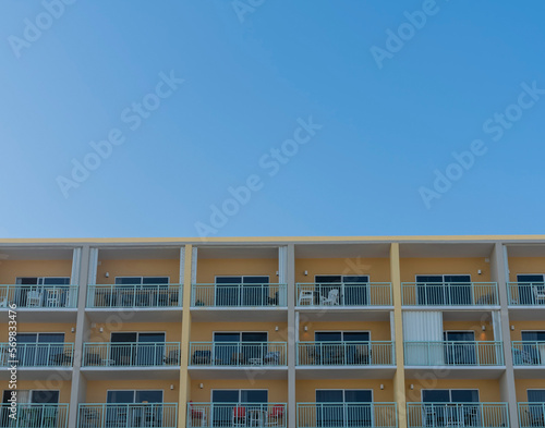Hotel or apartment building facade with square balconies against blue sky in Destin, Florida. Multi-storey building with white balcony railings and painted yellow wall exterior below the clear sky.