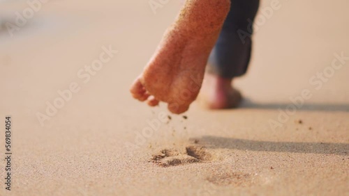 Closeup shot of footprint on the sand of the Kakolem beach with defocused man walking in background at Goa, India. Selective focus on the footprint left behind by the man walking barefoot on the beach