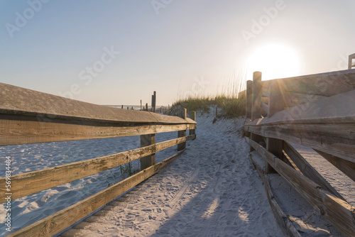Sand pathway with wooden railings near the sand dunes in Destin, Florida. Sunset light above the grassy sand dunes view from a walkway with sand and railings.