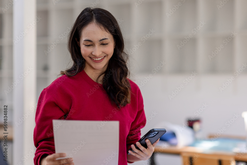 Portrait of an attractive young Indian beautiful Asian female holding her smartphone while working in a workplace. business finance concept Portrait of an attractive young Indian beautiful Asian female holding her smartphone while working in a workplace. business finance concept