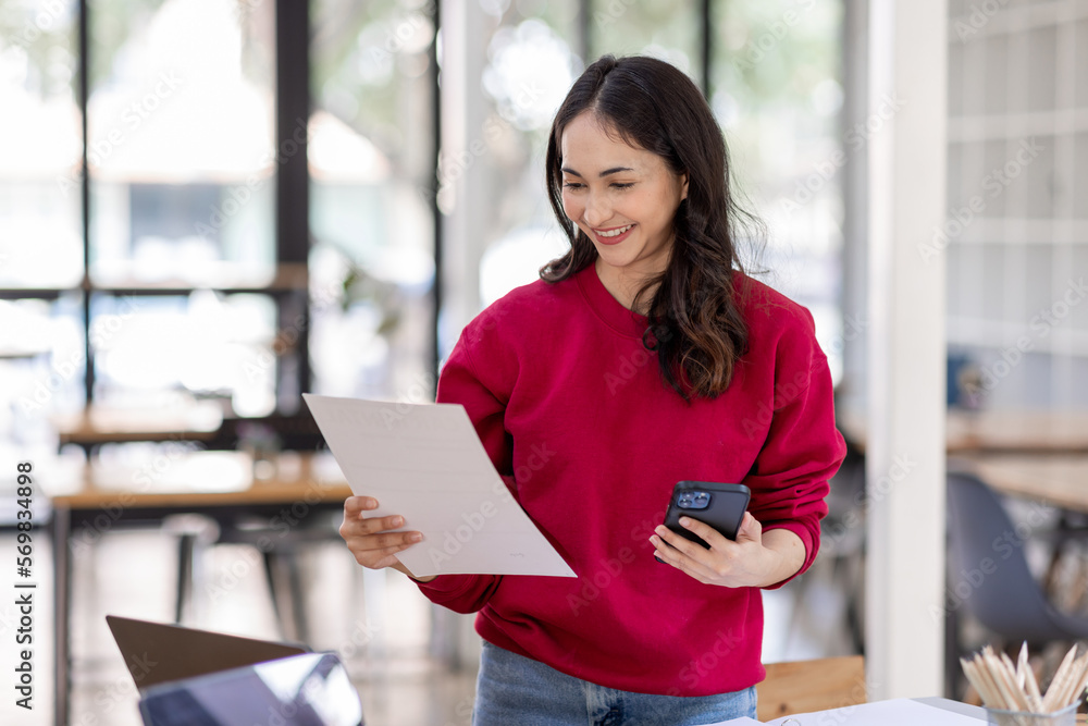 Portrait of an attractive young Indian beautiful Asian female holding her smartphone while working in a workplace. business finance concept Portrait of an attractive young Indian beautiful Asian female holding her smartphone while working in a workplace. business finance concept