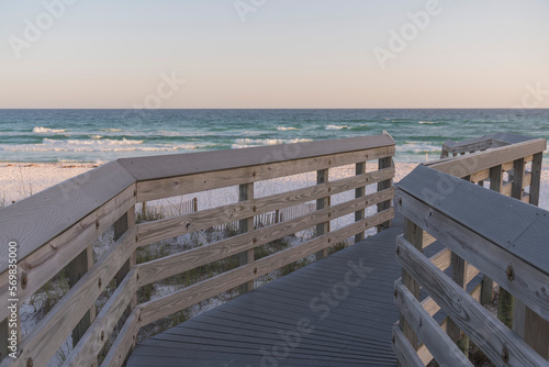 Wooden walkway turning to the right on a beach at Destin, Florida. View of a blue ocean below the horizon skyline background from the footbridge above sand dunes with fences.