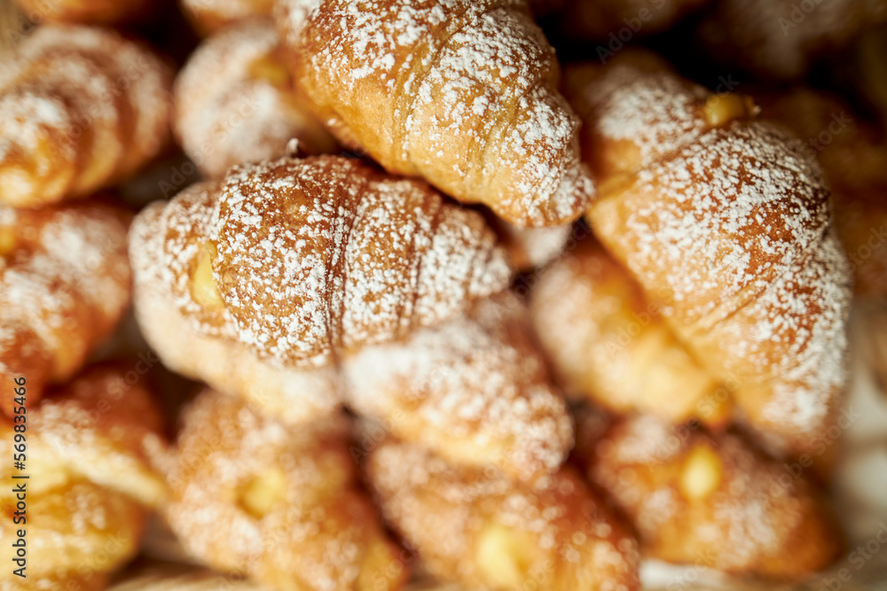 sweet croissants sprinkled with powdered sugar, top view. baked croissants sprinkled with powdered sugar on a wooden board. Close up croissants sprinkled with powdered sugar.