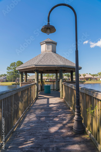 Wooden pathway with railings and hook post light at Navarre, Florida. Pathway heading to a gazebo with views of the lake at the front of the houses at the back.