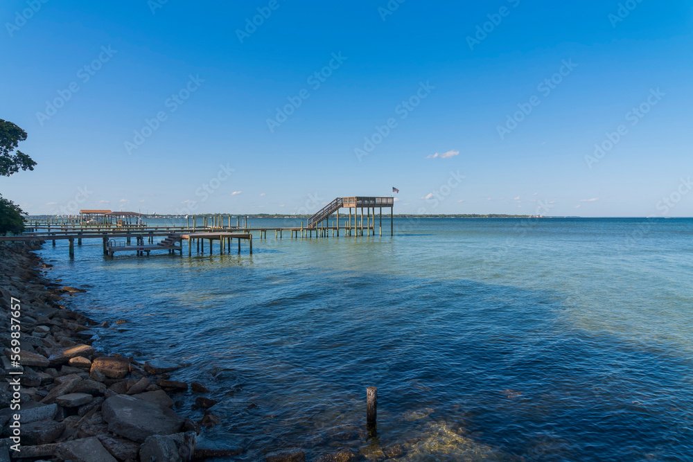 Wooden pier and dock at the bay in Navarre, Florida. Views from the shore with rocks of docks with view decks against the clear blue skyline background.