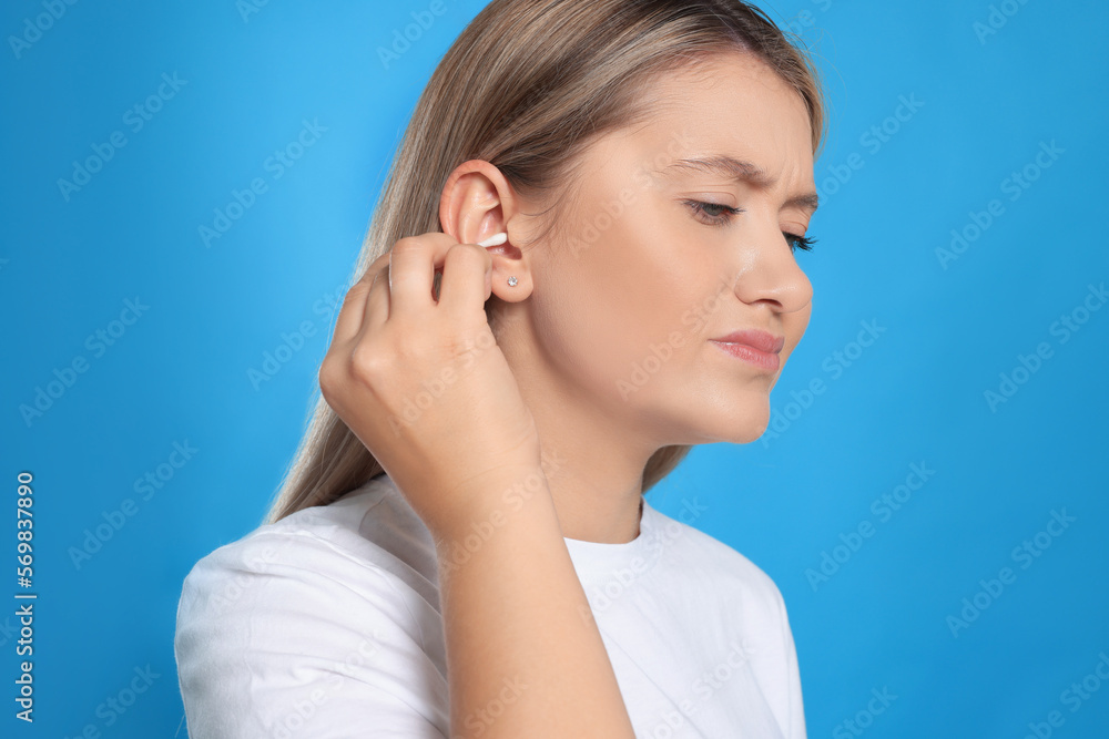 Young woman cleaning ear with cotton swab on light blue background Young woman cleaning ear with cotton swab on light blue background