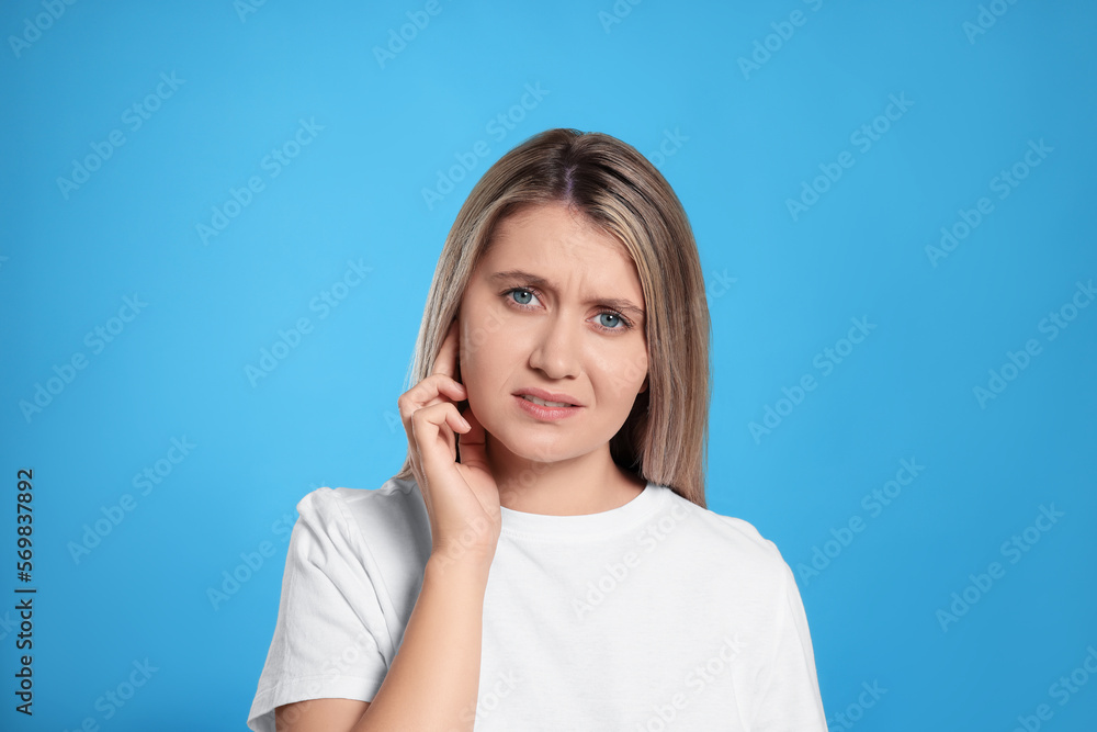 Young woman suffering from ear pain on light blue background Young woman suffering from ear pain on light blue background
