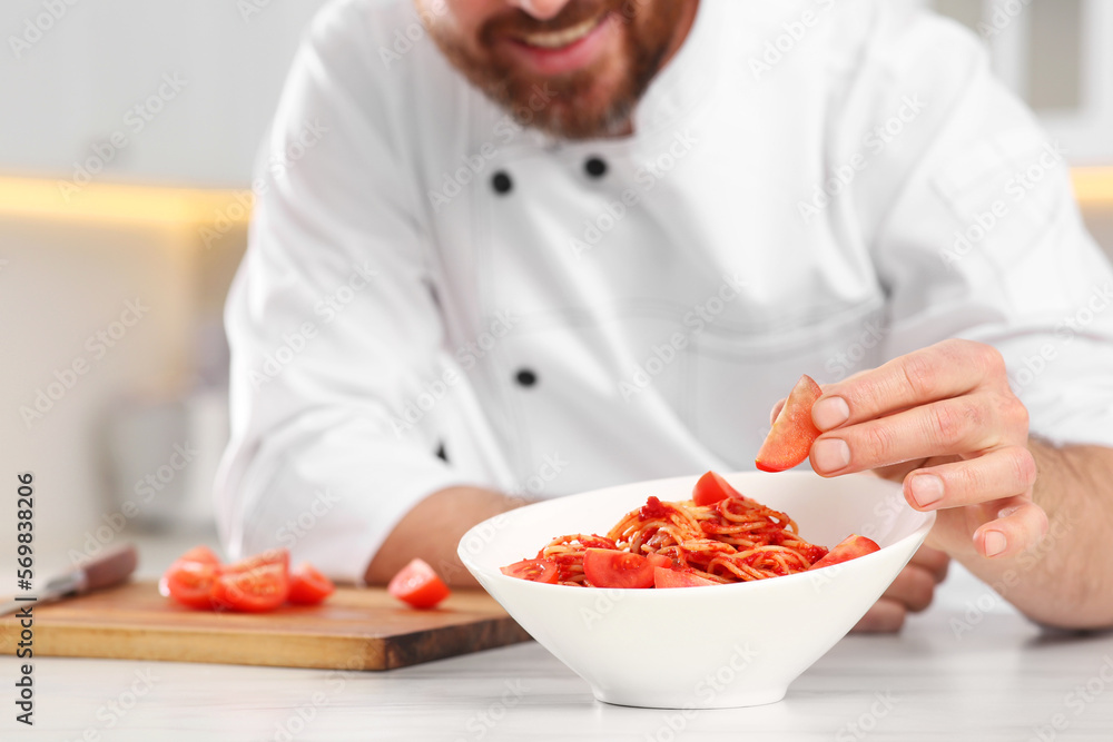 Closeup of professional chef adding tomato into bowl with delicious spaghetti at marble table in kitchen, focus on food