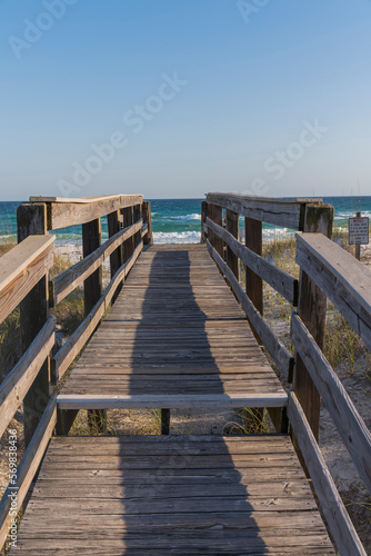 Wooden footbridge with step and railings heading to the beach at Destin  Florida. Footbridge over the sand dunes with notice sign on the right and views of ocean and skyline background.