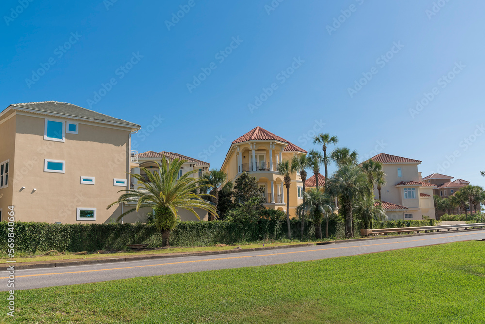 Views of a neighborhood behind a wall across the road in Destin, Florida. There is a lawn at the front near the road and vine-covered wall of houses across against the blue sky background. Views of a neighborhood behind a wall across the road in Destin, Florida. There is a lawn at the front near the road and vine-covered wall of houses across against the blue sky background.