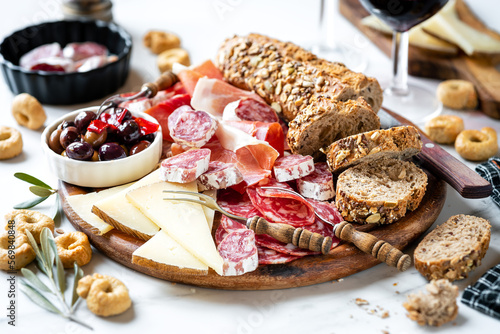 Meat and cheese platter with bread slices, typical Spanish tapas with serrano ham, fuet sausage, salami, goat chees, spicy olives and fresh bread and wine photo