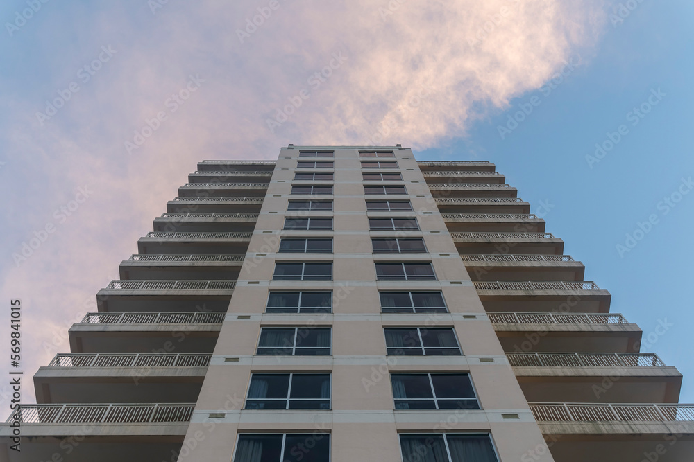 Low angle view of an apartment hotel building in Destin, Florida under the giant clouds. Multi-storey building exterior with balconies on both corners and paned picture windows in the middle. Low angle view of an apartment hotel building in Destin, Florida under the giant clouds. Multi-storey building exterior with balconies on both corners and paned picture windows in the middle.