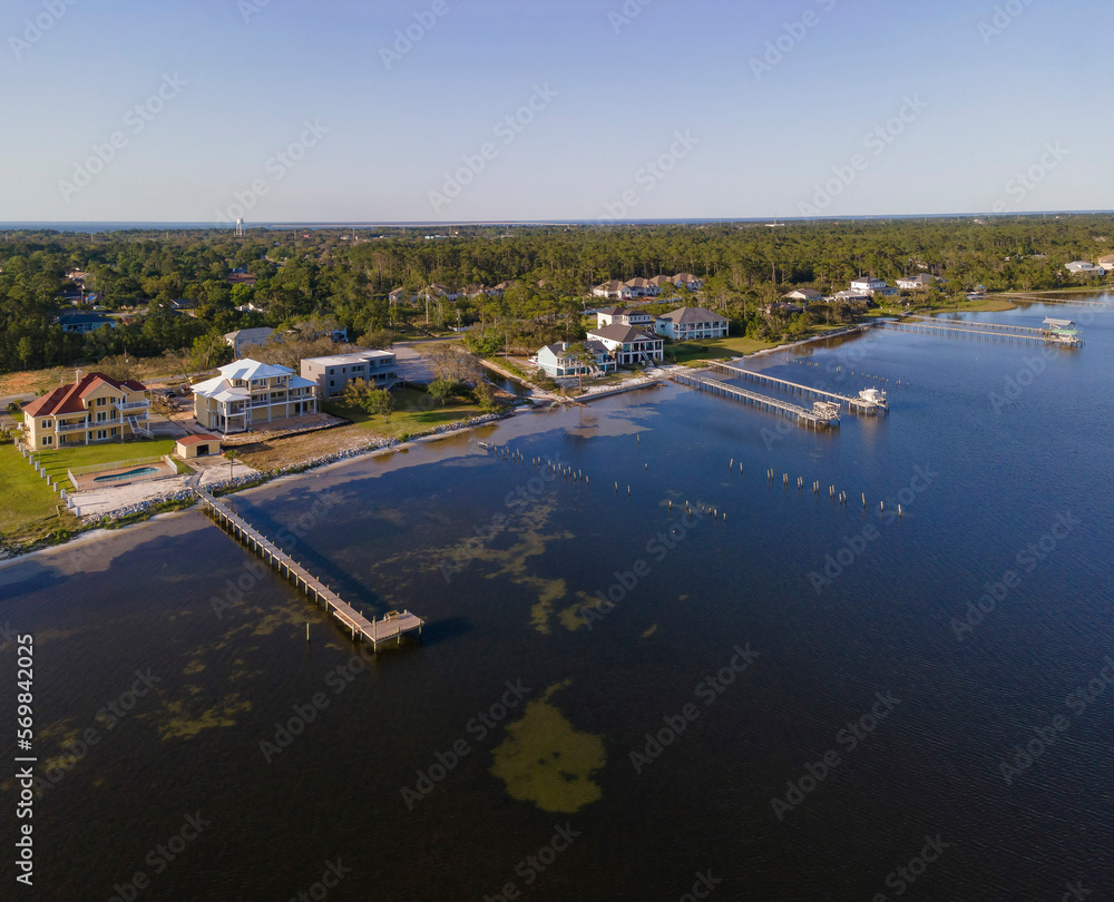 Aerial shot view of coastal villas with private docks in Navarre, Florida. Blue waterfront of villas with green tall trees surrounding the neighborhood and a view of clear skyline background.
