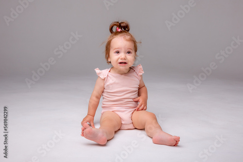 healthy baby girl in a pink bodysuit sits on a white background. space for text