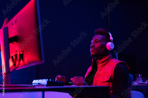 Young African man playing video game on computer. Streamer guy sitting at home and plays another match