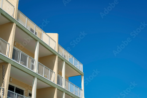 Building with painted cream walls, white balcony railings, and green trims- Destin, Florida. Low angle view of an apartment building under the clear blue sky.