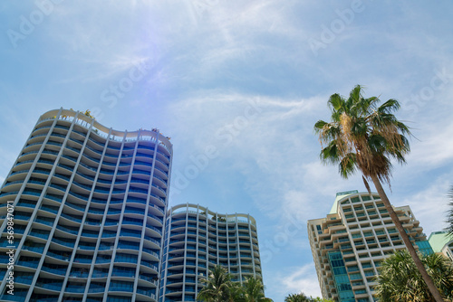 Low angle view of high rise condominiums with modern exterior at Miami, Florida. There are buildings on the left with curved structures and roof decks with trees near the white building on the right. © Jason