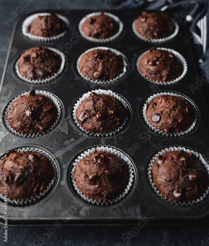 Close up of tin of chocolate zucchini muffins on black background.
