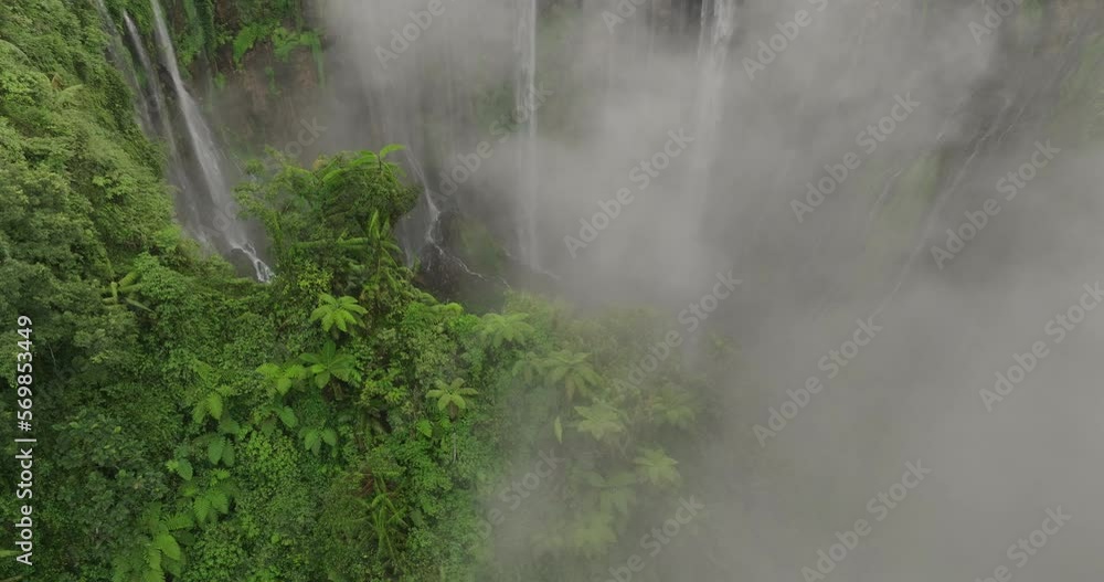Aerial Panning Scenic Shot Of Waterfall Seen Through Cloud, Drone Descending By Green Plants In Forest - Java, Indonesia Aerial Panning Scenic Shot Of Waterfall Seen Through Cloud, Drone Descending By Green Plants In Forest - Java, Indonesia