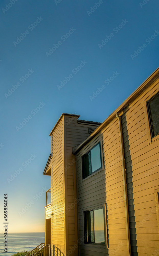 House exterior against sea and sky at sunset in Del Mar Southern California. Facade of a beach home with sunlit walls and view of the calm beach and golden horizon.