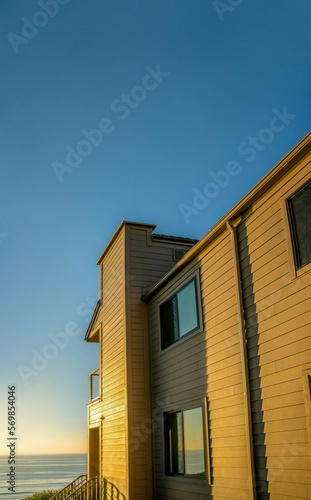 House exterior against sea and sky at sunset in Del Mar Southern California. Facade of a beach home with sunlit walls and view of the calm beach and golden horizon. © Jason