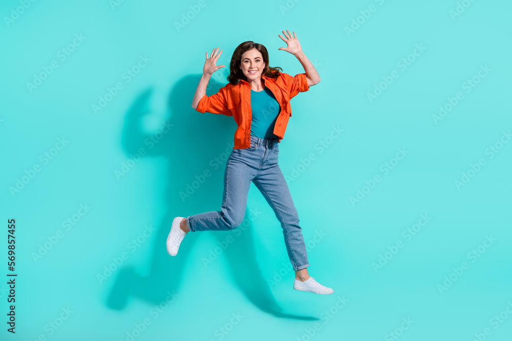 Full length photo of shiny sweet lady wear orange shirt jumping high isolated teal color background