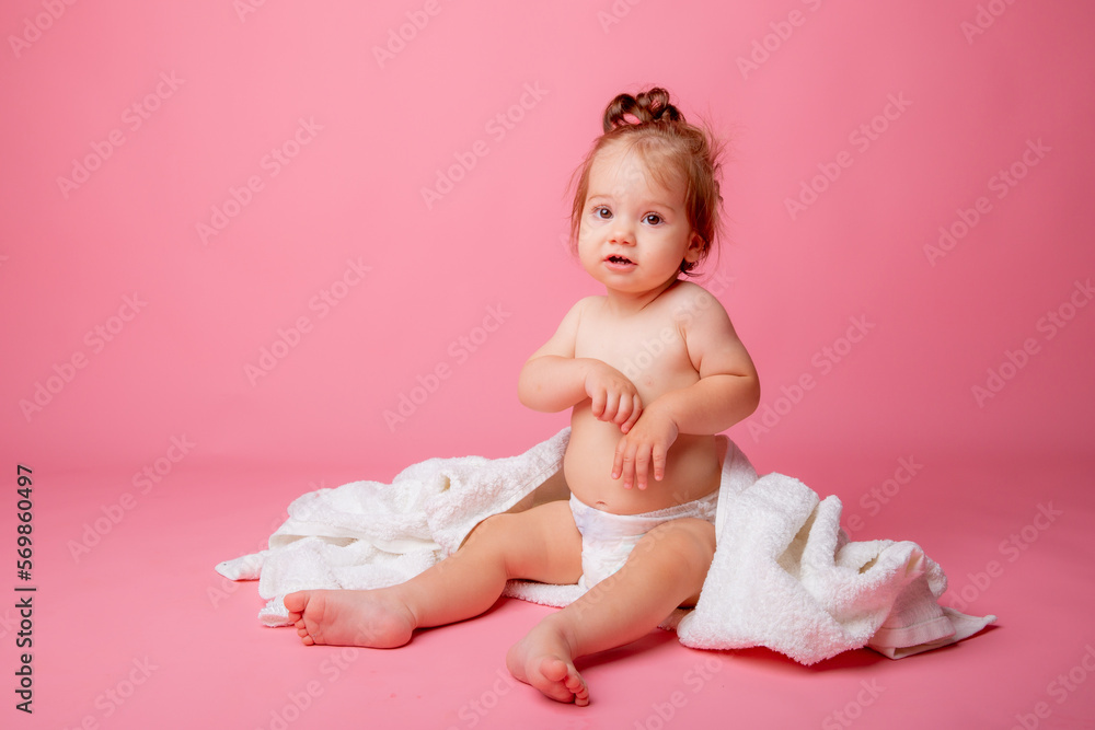 baby girl in a diaper wrapped in a towel sitting on a pink background, bathing concept baby girl in a diaper wrapped in a towel sitting on a pink background, bathing concept