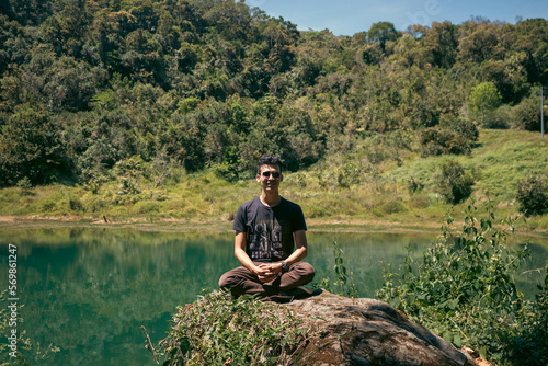 Hombre joven sentado sobre una piedra con lago de fondo