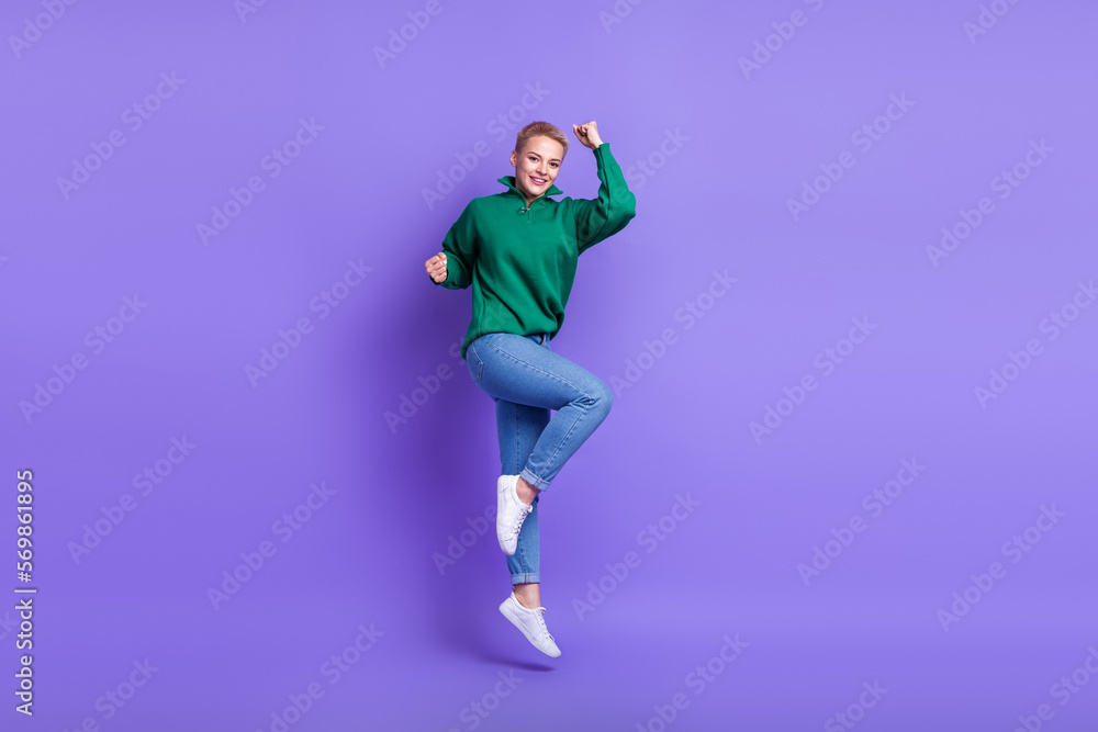 Full length photo of shiny lucky woman dressed green pullover jumping high rising fists isolated purple color background