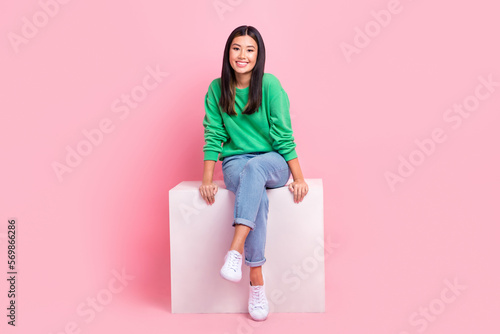 Full size portrait of gorgeous satisfied filipino girl sitting podium cube isolated on pink color background