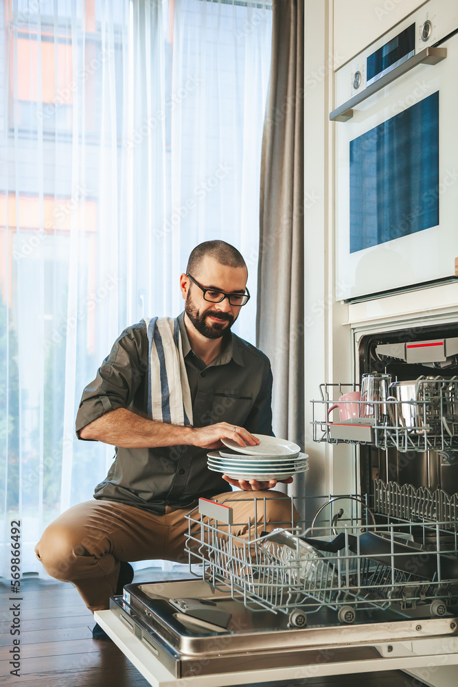 Smiling man unloading dishwasher Smiling man unloading dishwasher