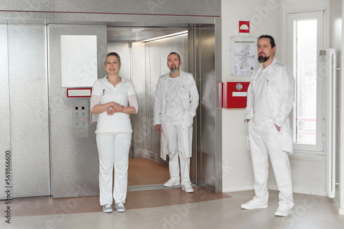 two doctors and a nurse stand at an elevator