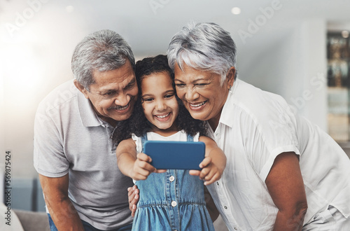 Love, happy and girl taking selfie with her grandparents in the lounge of modern family home. Happiness, smile and excited child taking picture with grandmother and grandfather at a house in Mexico. photo