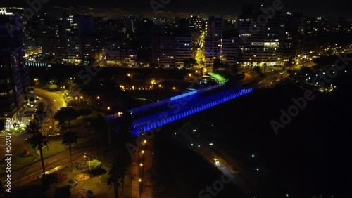 Night time 4k footage of a bridge being lit with LED color changing lights. Many city lights shine in distance. Many tall buildings in the background. Located in Miraflores district of Lima, Peru photo