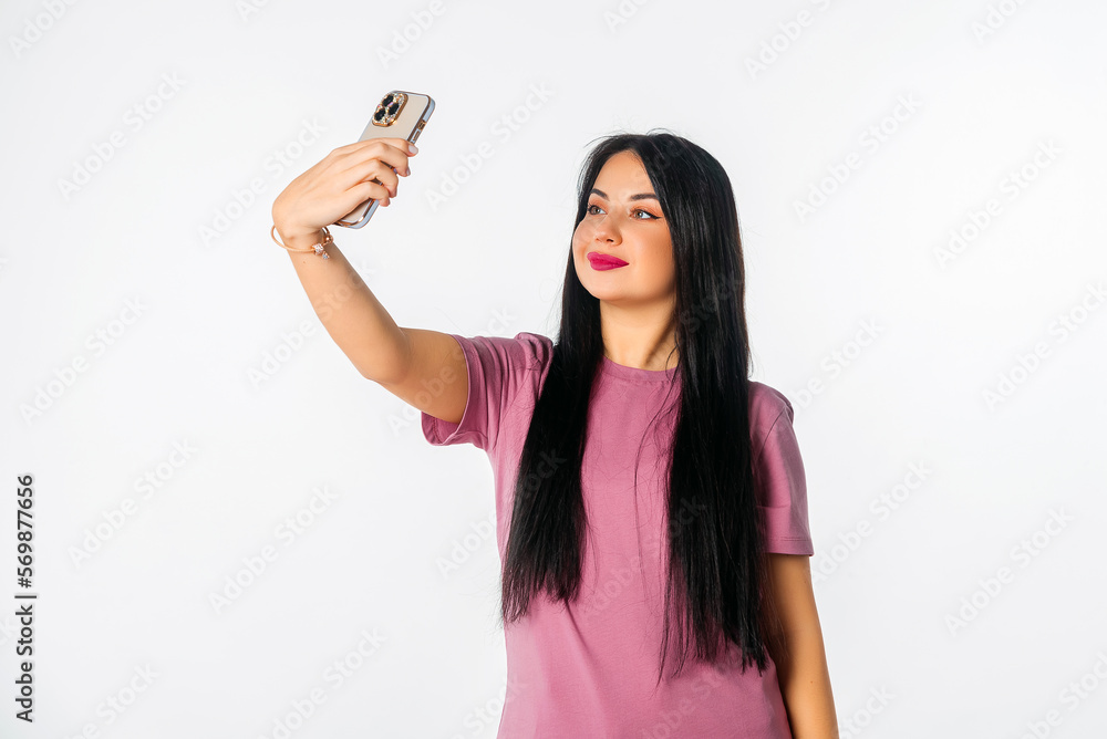 Lovely young woman holding smartphone using mobile phone app for video call or selfie photo, standing against white studio background Lovely young woman holding smartphone using mobile phone app for video call or selfie photo, standing against white studio background